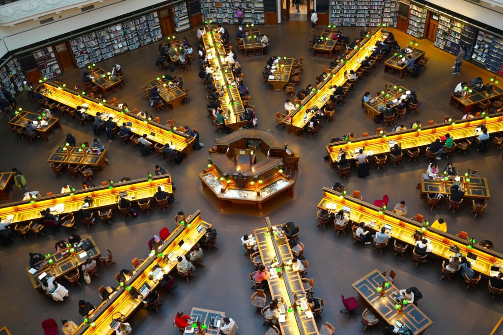A vibrant scene of people studying in the iconic State Library of Victoria's reading room.