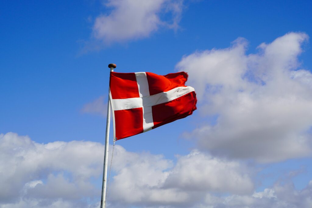 Danish flag waving proudly against a blue sky with fluffy clouds, symbolizing national pride.