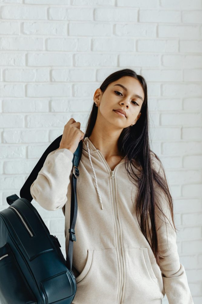 pexels-photo-8005444-8005444 Confident teenager with a backpack and hoodie poses against a white brick wall.